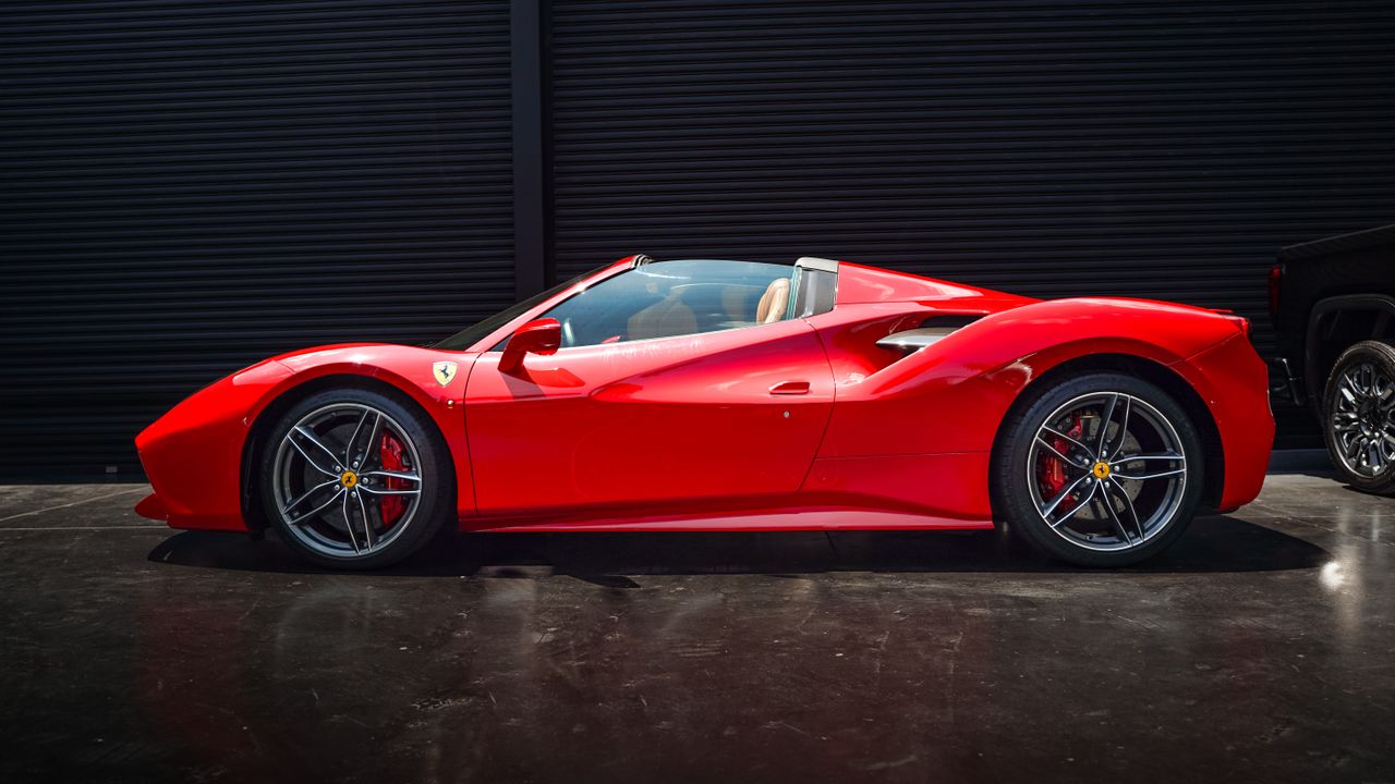 Sleek red Ferrari Spider supercar against a black background in an urban environment.